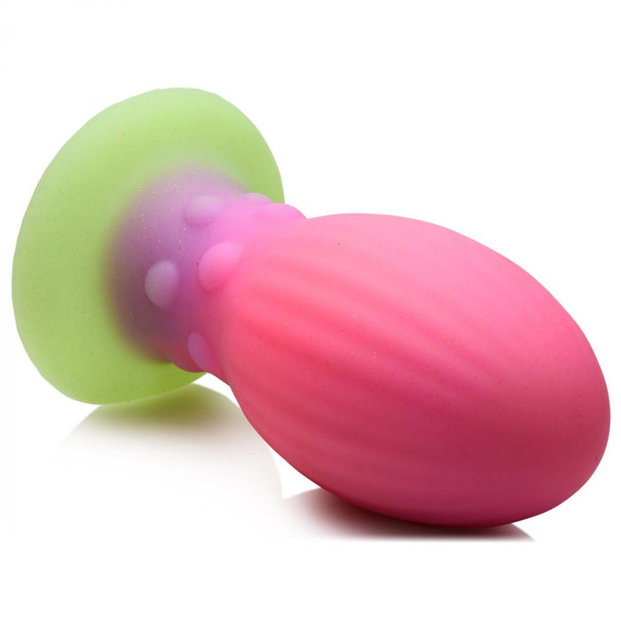 The Xeno Egg Glow In The Dark Extra Large Silicone Egg by XR Brands features a colorful silicone design with a ribbed pink bulbous head, a purple intermediate section with small bumps, and a green flared base for safe use. Crafted from premium silicone, its surface has a slight sheen that reflects light.