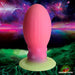 Introducing the Xeno Egg Glow In The Dark Extra Large Silicone Egg by XR Brands, this fantasy-themed toy features an abstract, stylized tentacle design with ribbed sides and a striking gradient from pink to green. The space-inspired backdrop showcases vibrant planets, stars, and nebulae, while the bottom right corner prominently displays the "Creature Cocks" logo.