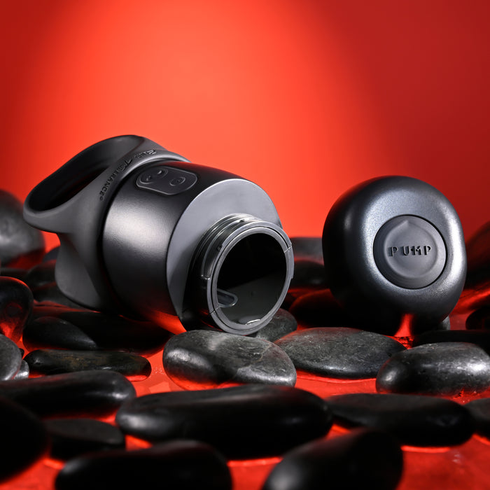 A sleek, gray Wet It Be Hand Held Vibrating Masturbator with Lube Dispenser, its cap removed, is placed on a bed of smooth black stones against a vivid red background. Both the masturbator and the cap feature the "Evolved Novelties" brand name engraved on them, making it your handy helper for intimate pleasure in style.