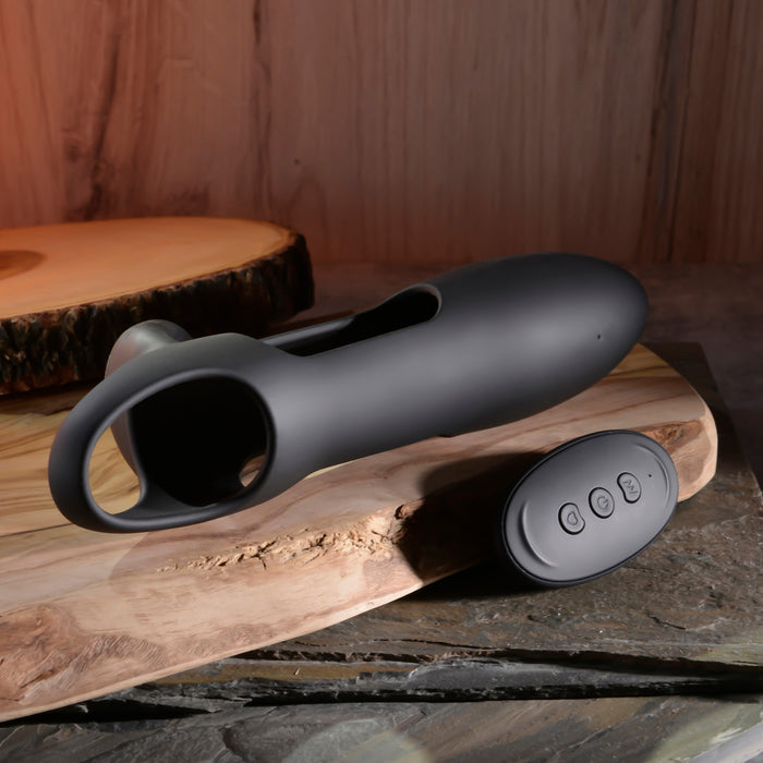 A sleek black Nautilus Rechargeable Vibrating Penis Sleeve for couples, with a handle, rests on wood next to its small oval three-button remote. The rustic wooden background enhances the charm of this flexible and stretchy design.