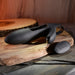 The Nautilus Rechargeable Vibrating Penis Sleeve for Couples, with its sleek black design and attached loop, sits elegantly on a wooden surface. Nearby, a small remote control with three buttons invites use, all under warm ambient lighting for an inviting atmosphere.