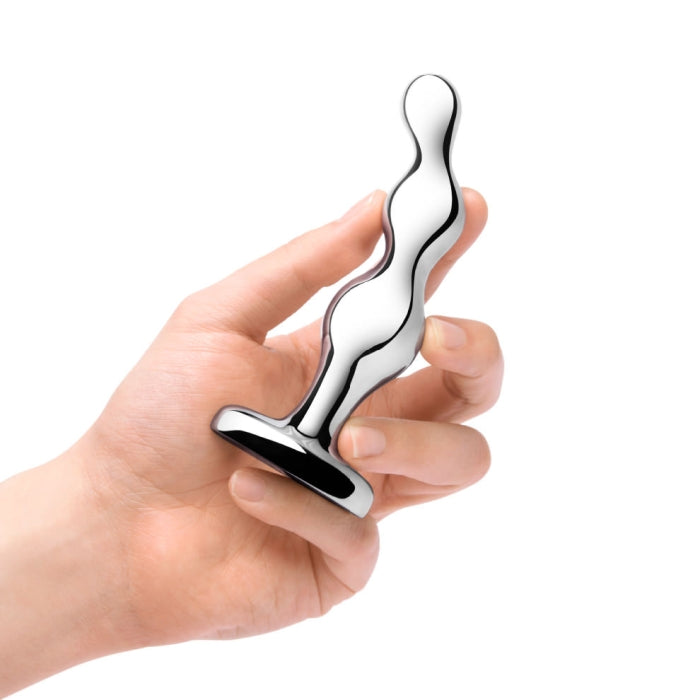 A hand holding the b-Vibe Stainless Steel Weighted Anal Beads for Prostate, a metallic, wavy-shaped object with a broad, flat base. This body-safe sex toy by b-Vibe features a sleek and reflective surface with multiple curves along its length, ideal for prostate stimulation. The background is plain white.