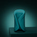 A sleek teal Lovense Gush 2 oscillating masturbator with smooth curves and a circular pattern stands on a dark surface against a gradient teal background, offering modern design and app compatibility for a hands-free experience.