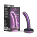 A shimmering purple curved dildo, ideal for exploration and pegging play, stands upright beside its packaging. The box highlights product details and displays the dildo image under the brand name "Blush." The toy boasts a rounded base to ensure steadiness during use.