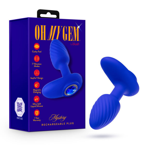 Presenting the "Mystery Vibrating Textured Silicone Butt Plug in Sapphire" by Blush – a blue silicone anal toy adorned with a gem-like end, showcased next to its eye-catching purple and blue packaging. The "Oh My Gem!" box emphasizes 7 vibration modes, magnetic charging, and a luxurious platinum cured silicone texture for unparalleled comfort and pleasure.