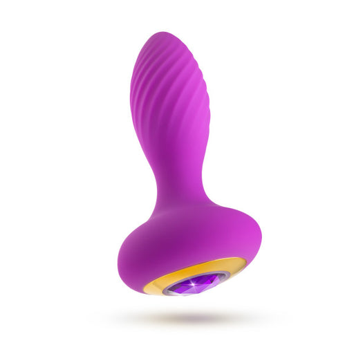 The Charm Vibrating Textured Silicone Butt Plug in Amethyst by Blush is crafted from purple platinum-cured silicone. It features a ridged, curved design and boasts a gold and purple jewel-like base. The product's vibrant color and unique shape are accentuated against the plain white background.